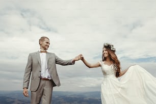 magnifique mariée et le marié se tenant la main et dansant au ciel et aux nuages, moment de vrai bonheur, cérémonie de luxe aux montagnes avec vue imprenable, espace pour le texte