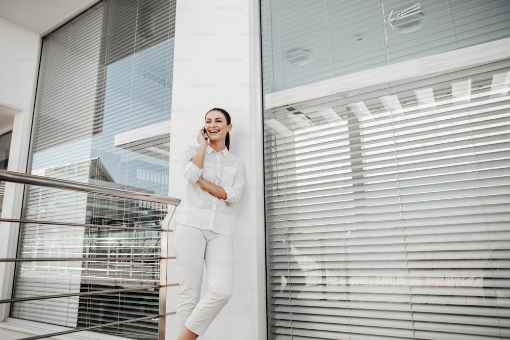 Low angle of glad female person standing outdoors and using gadget for communication. She is laughing. Copy space in right side