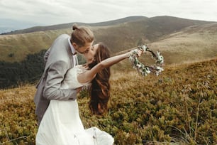 Stilvoller Bräutigam, der wunderschöne Braut im Sonnenlicht küsst, perfekter Moment, Boho-Hochzeitspaar, Luxuszeremonie in den Bergen mit herrlicher Aussicht