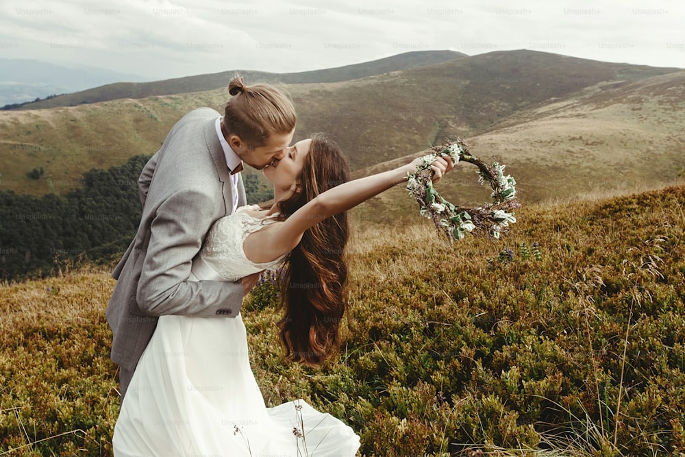novio elegante besando a la hermosa novia a la luz del sol, momento perfecto, pareja de bodas boho, ceremonia de lujo en las montañas con vista increíble