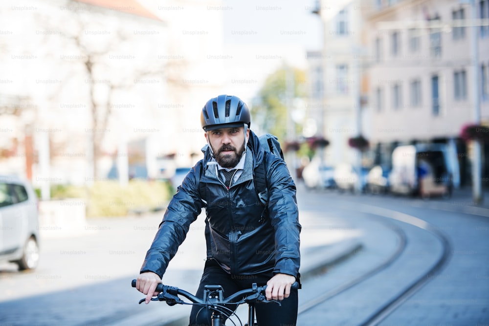 Eine Vorderansicht von Hipster-Geschäftsmann Pendler mit Fahrrad, der zur Arbeit in der Stadt fährt.