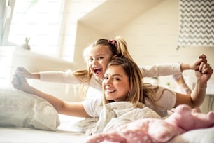 Mother and daughter having piggyback ride in bed. Portrait.