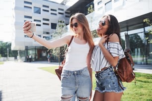 Two beautiful happy young student girl with backpack near the campus of university. Education and leisure concept.