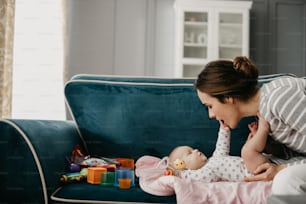 Senhora sorridente e alegre olhando para o bebê enquanto se senta no sofá dentro de casa. Conceito de maternidade feliz
