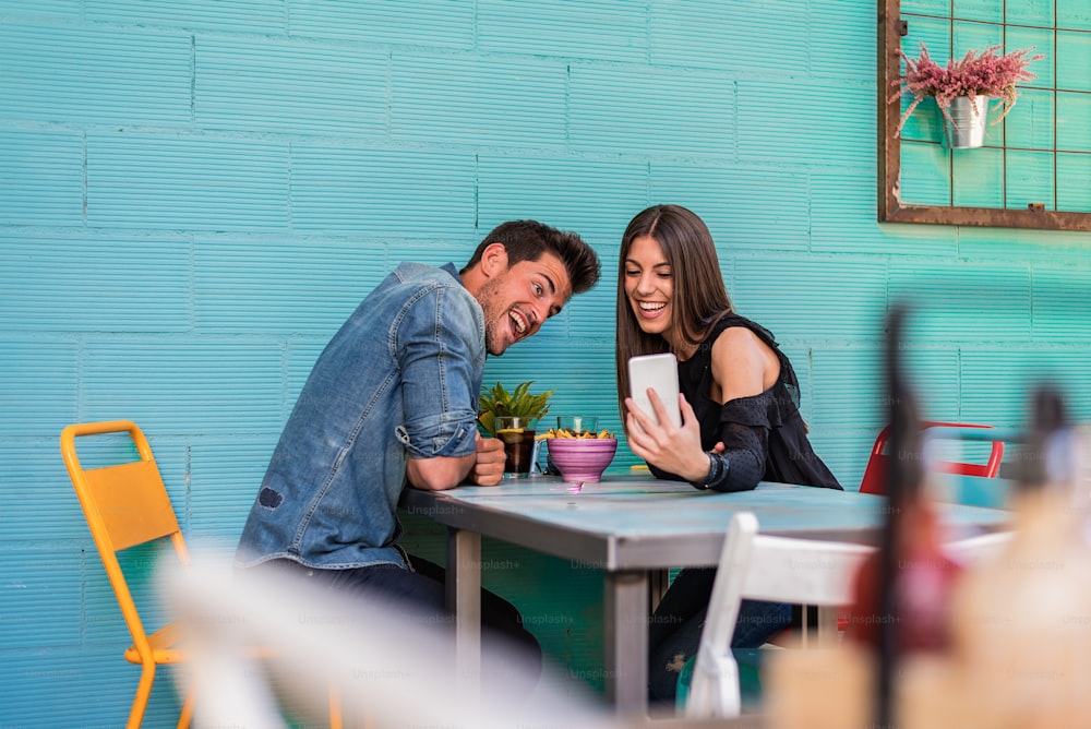 Happy young couple seating in a restaurant with a smartphone