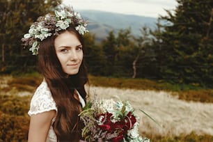 stylish bride posing with bouquet on background of forest, luxury gorgeous boho wedding at mountains
