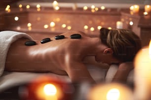 Concept of relaxation and body care. Waist up portrait of young woman having relaxing massage with warm stones in beauty and spa salon