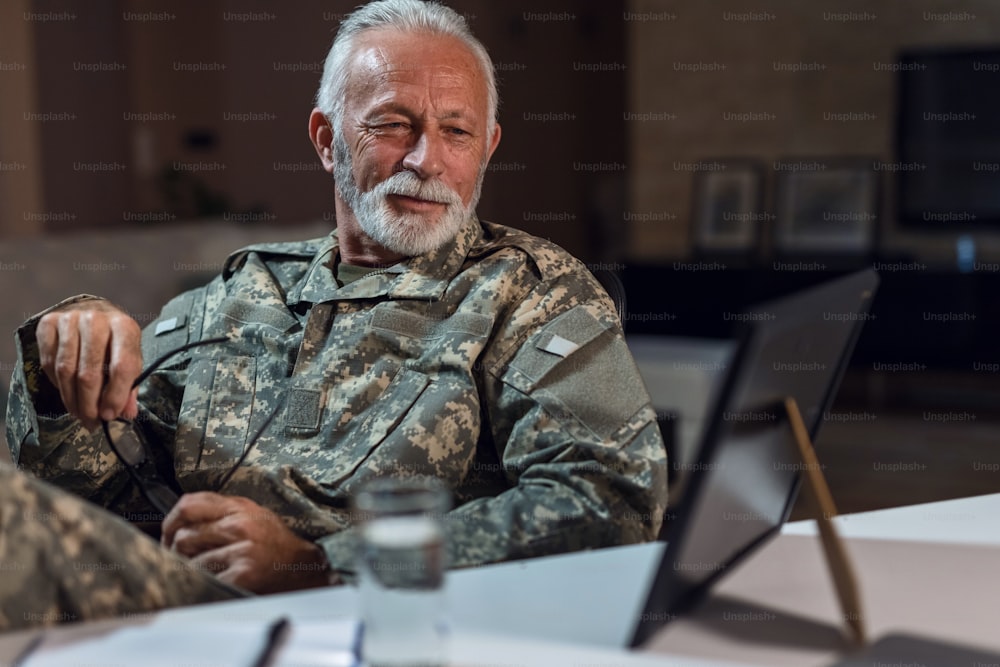 Lächelnder Soldat in Militäruniform, der auf ein gerahmtes Foto auf seinem Schreibtisch schaut und sich nostalgisch fühlt.