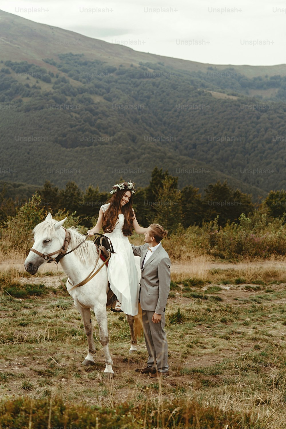 magnifique mariée chevauchant un cheval blanc et élégant marié, couple de mariage boho, cérémonie de luxe à la montagne, espace pour le texte