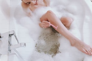 Mulher jovem alegre tomando banho enquanto raspa as pernas