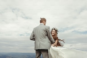 splendida sposa e sposo che si tengono per mano e ballano al cielo e alle nuvole, momento di vera felicità, cerimonia di lusso in montagna con vista mozzafiato, spazio per il testo
