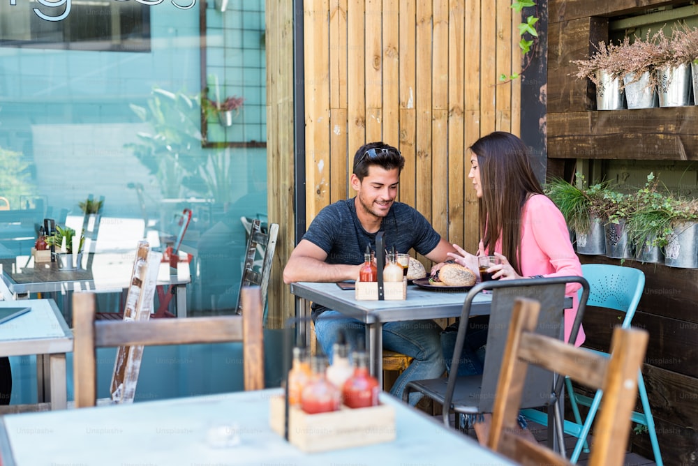 Giovane coppia felice che si siede sulla terrazza di un ristorante che mangia un hamburger