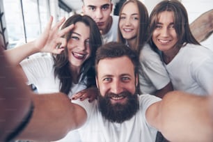 A group of people make a selfie photo in a cafe. The best friends gathered together at a dinner table eating pizza and singing various drinks.