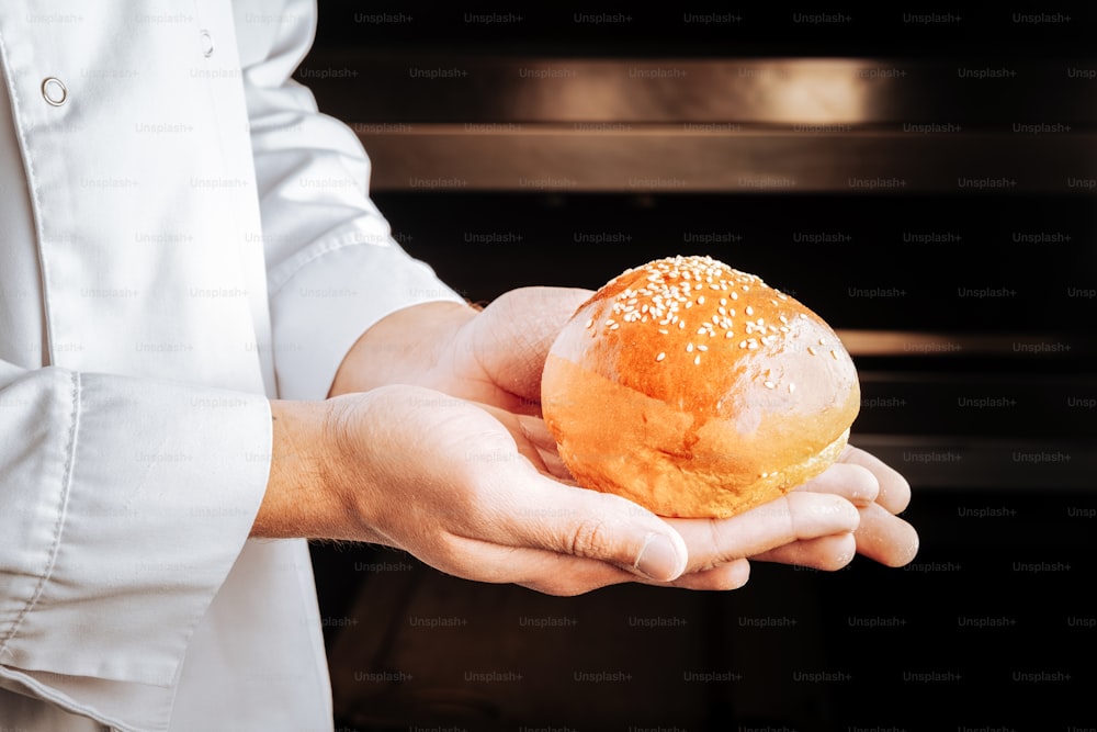 With sesame seeds. Little white bun topped with sesame seeds on palms of baker wearing white uniform