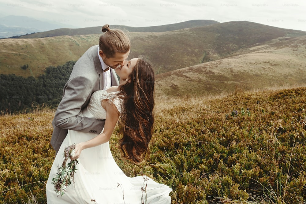 stylish groom  kissing gorgeous bride in sun light, perfect moment, boho wedding couple, luxury ceremony at mountains with amazing view