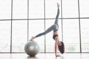 Sport ist eine Frau, die Yoga-Kurse macht und ihre Beine auf dem Ball in der Nähe des großen Fensters ausstreckt.