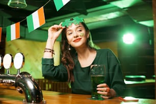 Tender smile. Long-haired cute girl in a green blouse smiling tenderly while wearing shamrock glasses