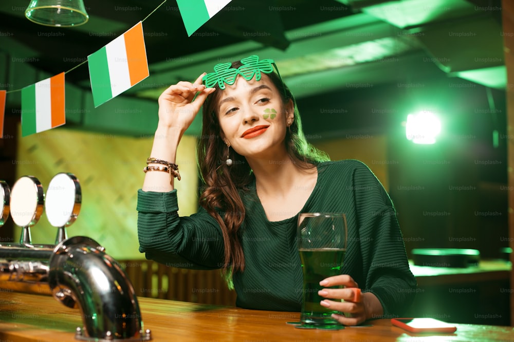 Tender smile. Long-haired cute girl in a green blouse smiling tenderly while wearing shamrock glasses