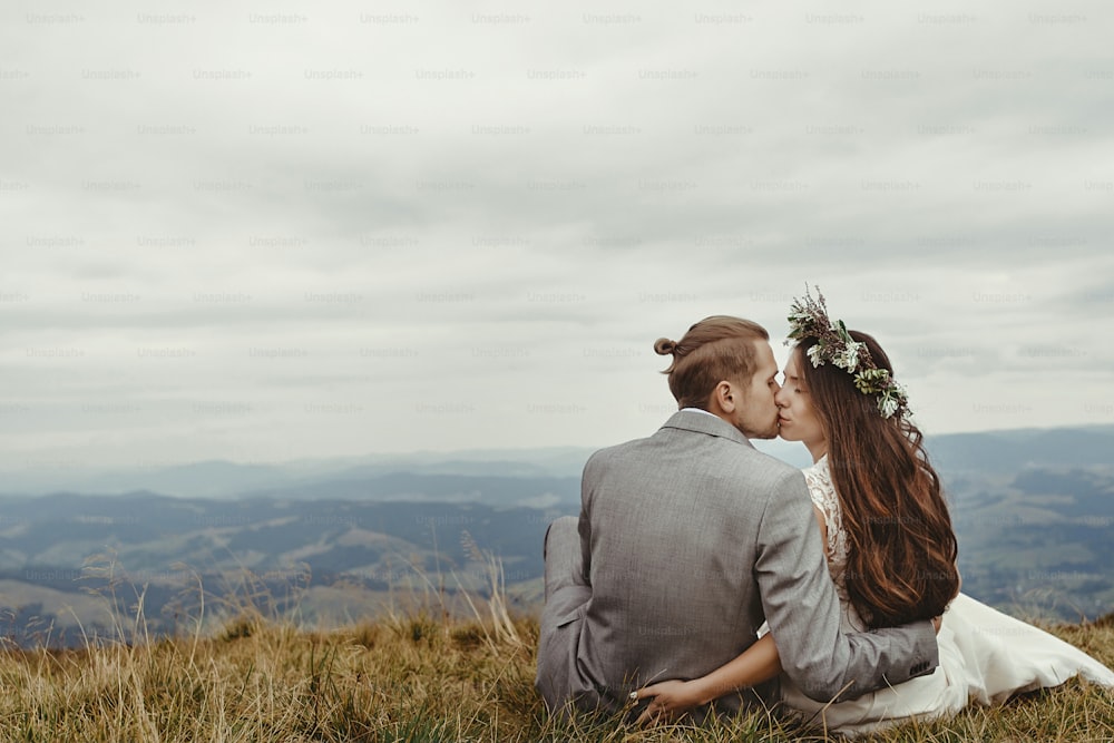 gorgeous bride and stylish groom kissing on top,  boho wedding couple, luxury ceremony at mountains with amazing view, space for text
