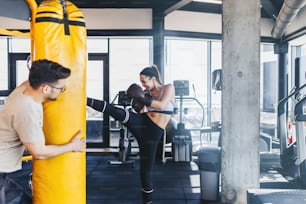 Young attractive woman with instructor on kickboxing training. She hitting or punching in big yellow boxing bag.