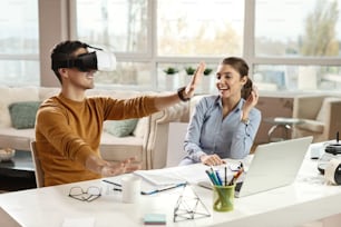 Joven empresario probando auriculares de realidad virtual y divirtiéndose con su colega en la oficina.