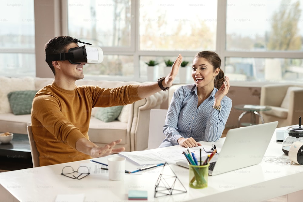 Young businessman testing virtual reality headset and having fun with his female colleague in the office.