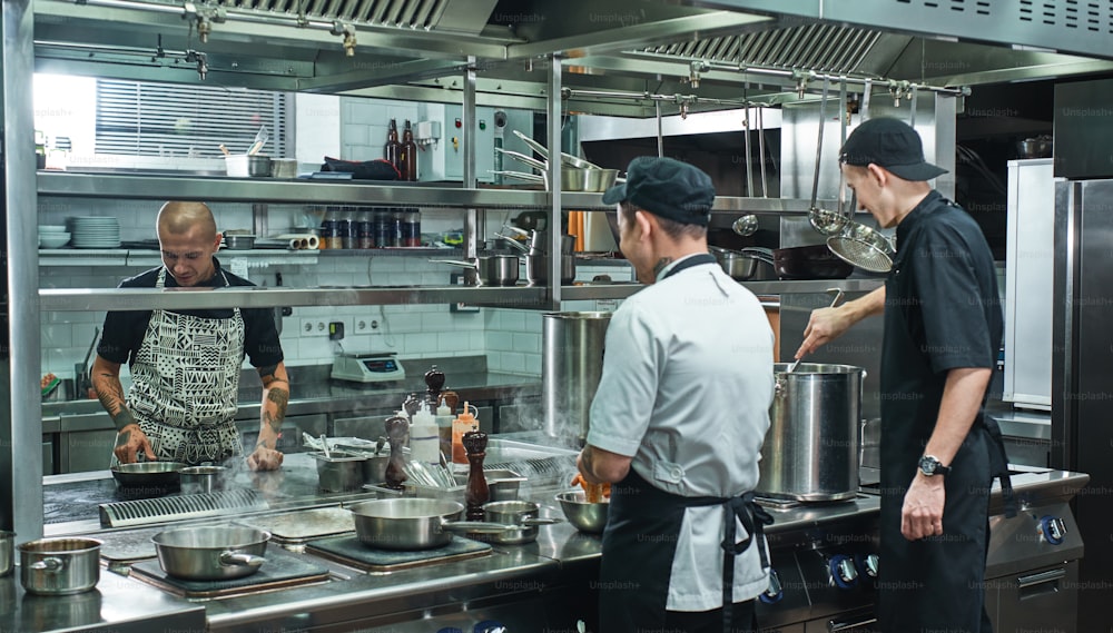 Cooking process. Professional team of chef and two young assistant preparing food in a restaurant kitchen. Teamwork
