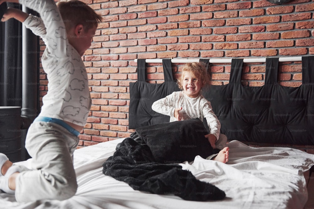 Crianças travessas Garotinho e menina encenaram uma briga de travesseiros na cama do quarto. Eles gostam desse tipo de jogo.