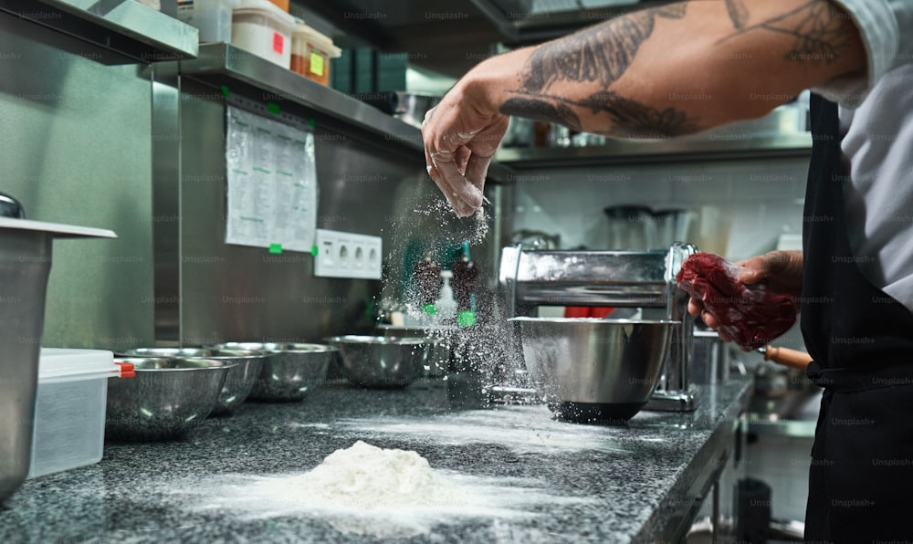 Processus de cuisson. Mains de chef masculin avec des tatouages noirs versant de la farine sur la table de la cuisine. Concept alimentaire