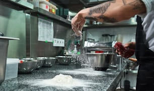 Cooking process. Male chef hands with black tattoos pouring flour on kitchen table. Food concept
