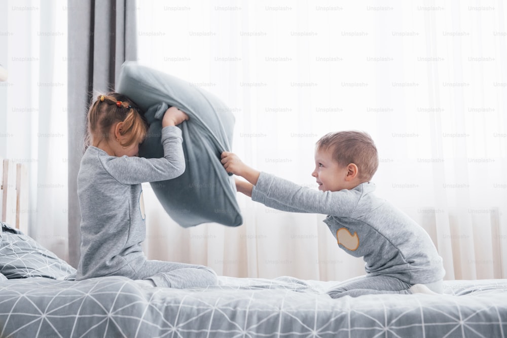 Menino e menina encenaram uma briga de travesseiros na cama do quarto. Crianças travessas batem umas nas outras travesseiros. Eles gostam desse tipo de jogo.