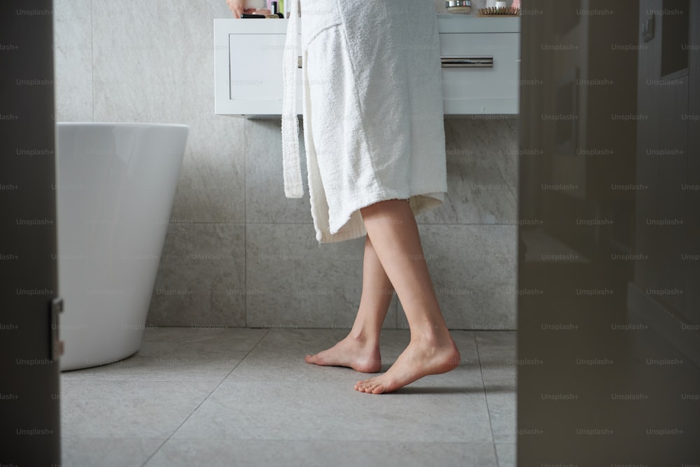 Selbstpflege- und Hygienekonzept. Porträt einer jungen, schlanken barfüßigen Frau, die im Badezimmer in der Nähe des Waschtisches wohnt