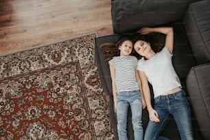Family spending time together. Top view portrait of happy smiling woman with her teenager child looking at camera while laying on sofa at home