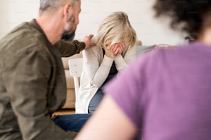 A senior depressed woman crying during group therapy, other people comforting her.