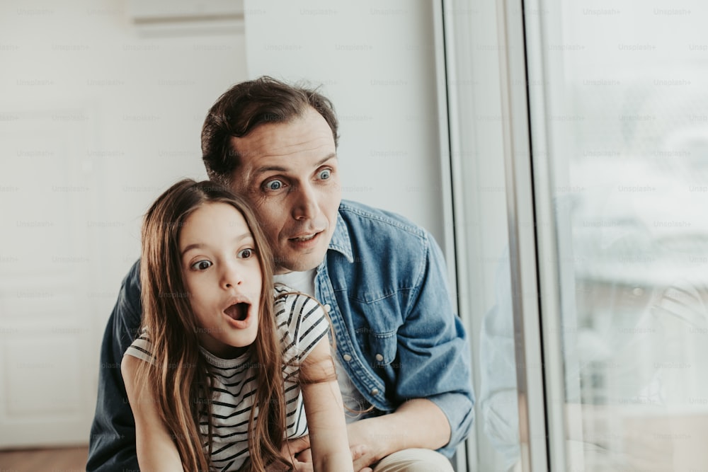 Family spending time together. Waist up portrait of very surprised man looking at something interesting with his female child on window at home