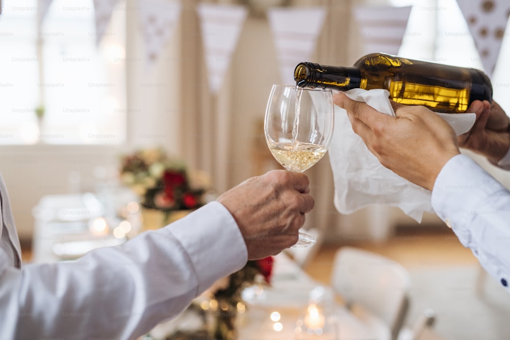 Une section médiane d’un homme méconnaissable versant du vin à des invités heureux lors d’une fête d’anniversaire familiale à l’intérieur.