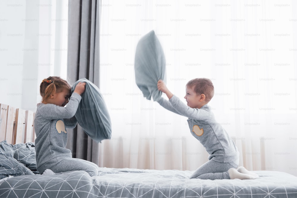小さな男の子と女の子は、寝室のベッドの上で枕投げをしました。いたずらっ子同士が枕を叩き合う。彼らはそのようなゲームが好きです。