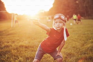 Bambino felice in casco da pilota che gioca con un aeroplano giocattolo di legno e sogna di diventare volante.