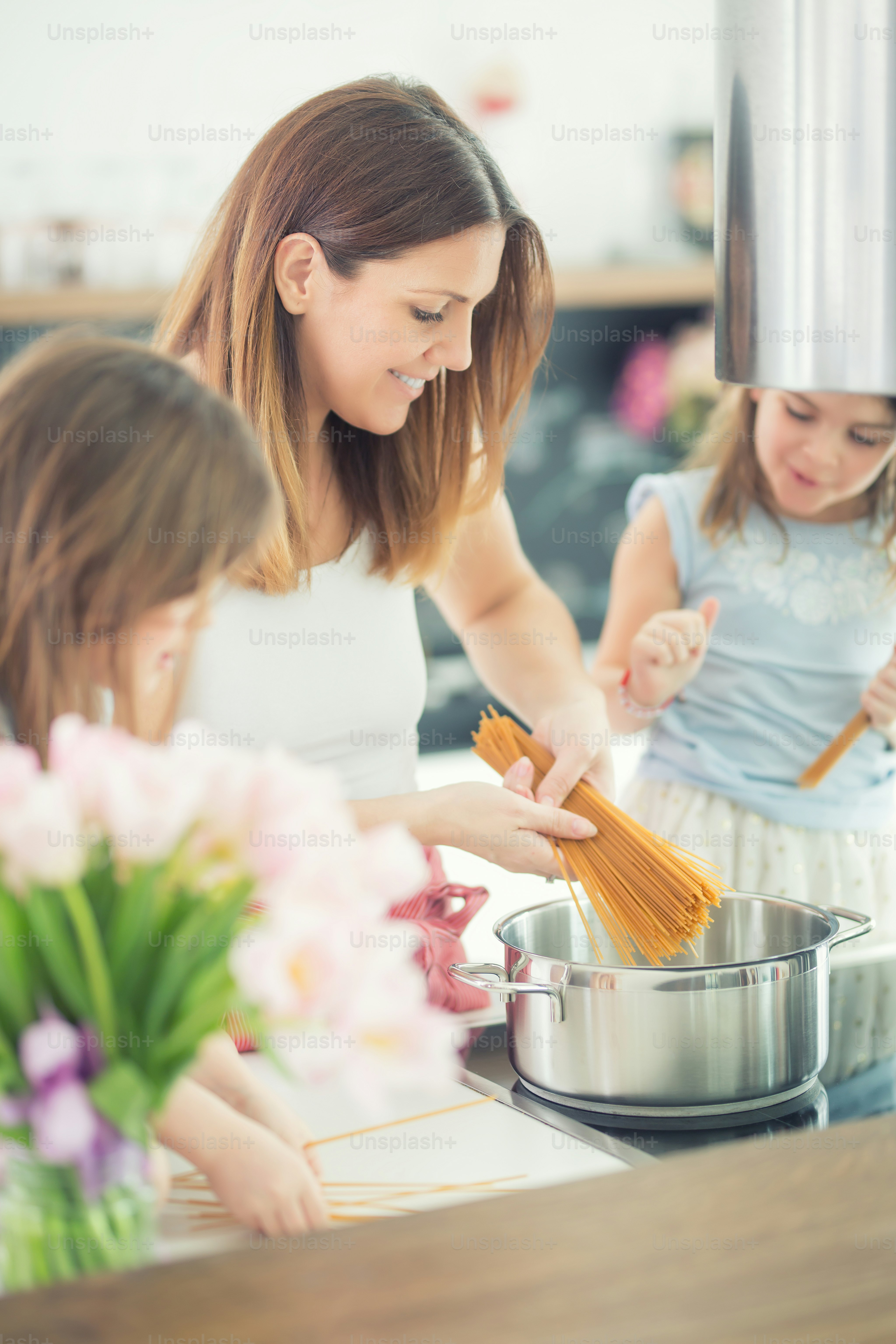 Mom with two young twins daughters in the kitchen cooking spaghetti.