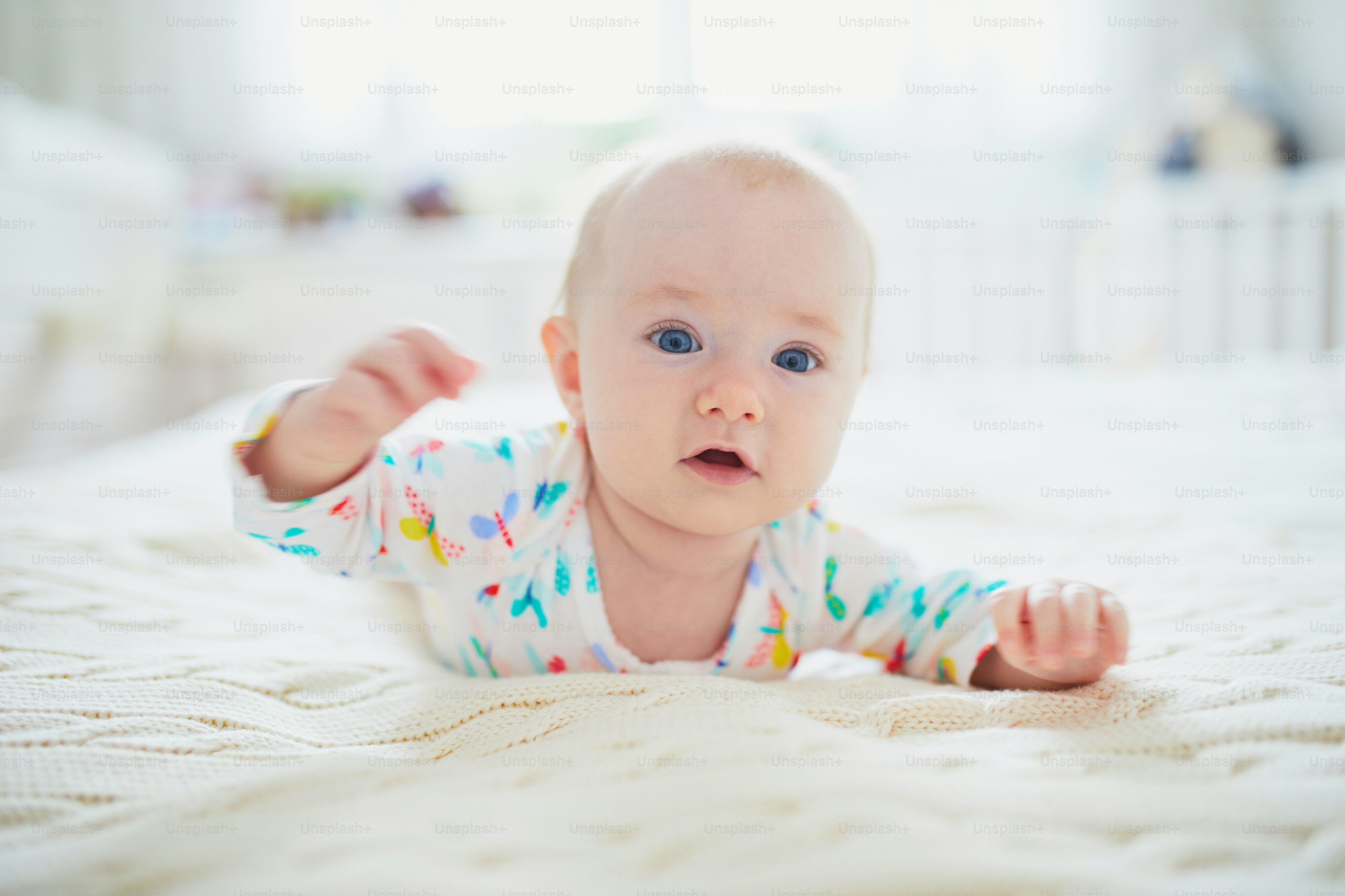Adorable baby girl lying on bed on her tummy. Happy healthy little