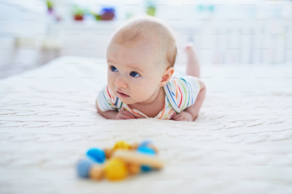 Adorable baby girl lying on bed on her tummy. Happy healthy little child practice crawling. Infant kid in sunny nursery doing tummy time