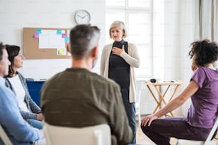 A senior woman standing and talking to other people during group therapy.