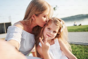 Giovane madre felice con una figlia giocosa in un parco vicino all'acqua.