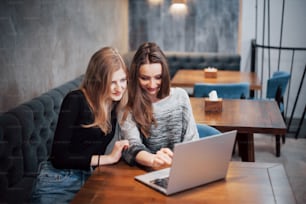 One-on-one meeting.Two young business women sitting at table in cafe.Girl shows colleague information on laptop screen.Meeting friends, dinner together.Teamwork, business meeting. Freelancers working.