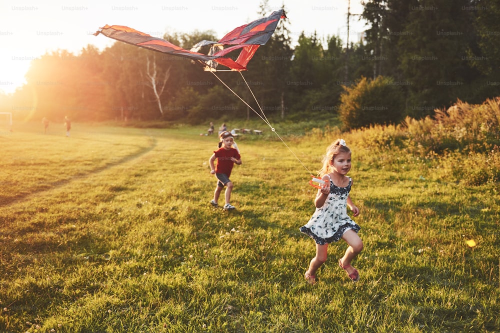 Des enfants heureux lancent un cerf-volant dans le champ au coucher du soleil. Petit garçon et petite fille en vacances d’été.