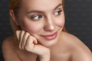 Beautiful young woman with natural makeup expressing joy and smiling while looking into the distance with her hand under the chin