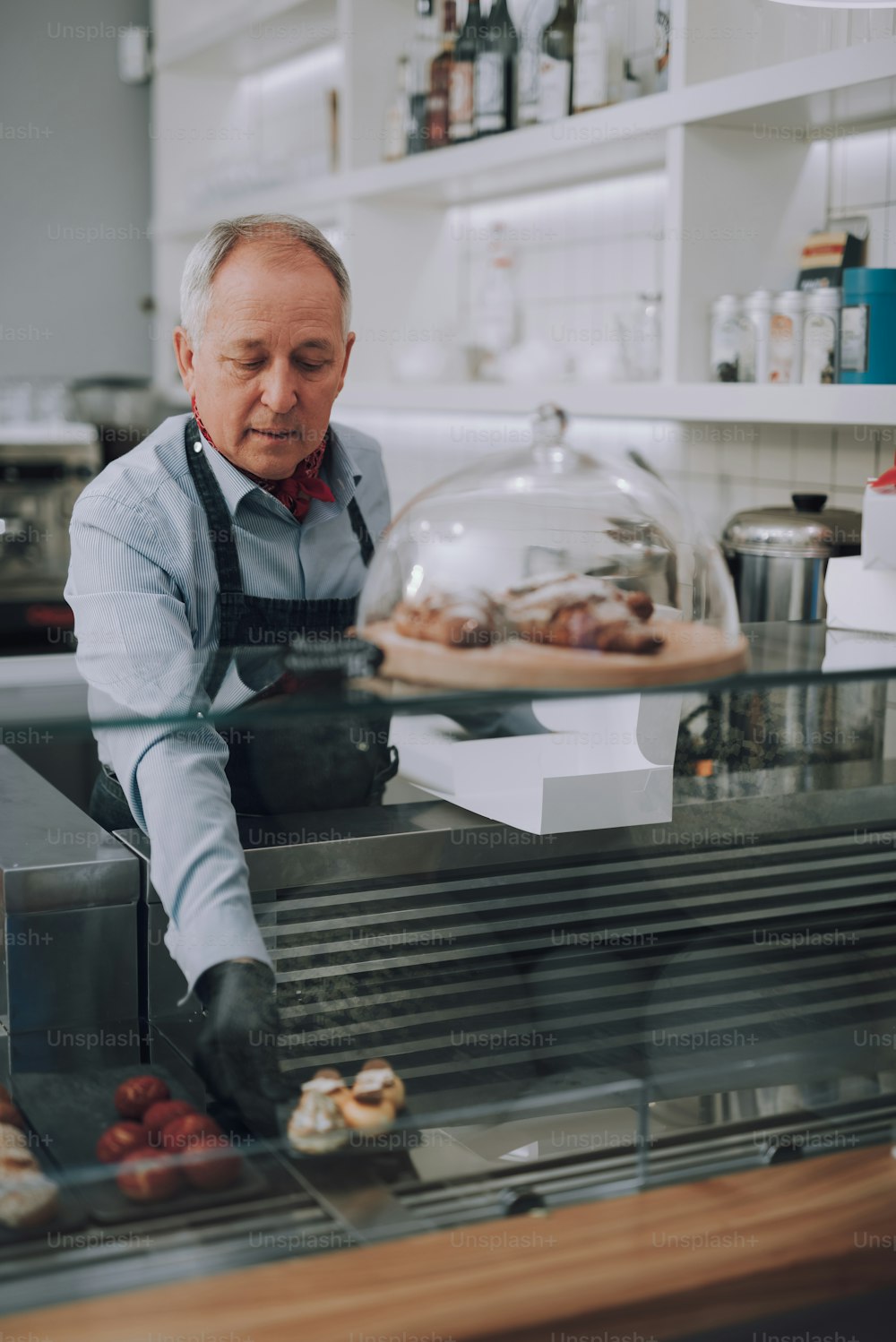 Vertical portrait of good-looking gentleman in apron placing cakes on showcase