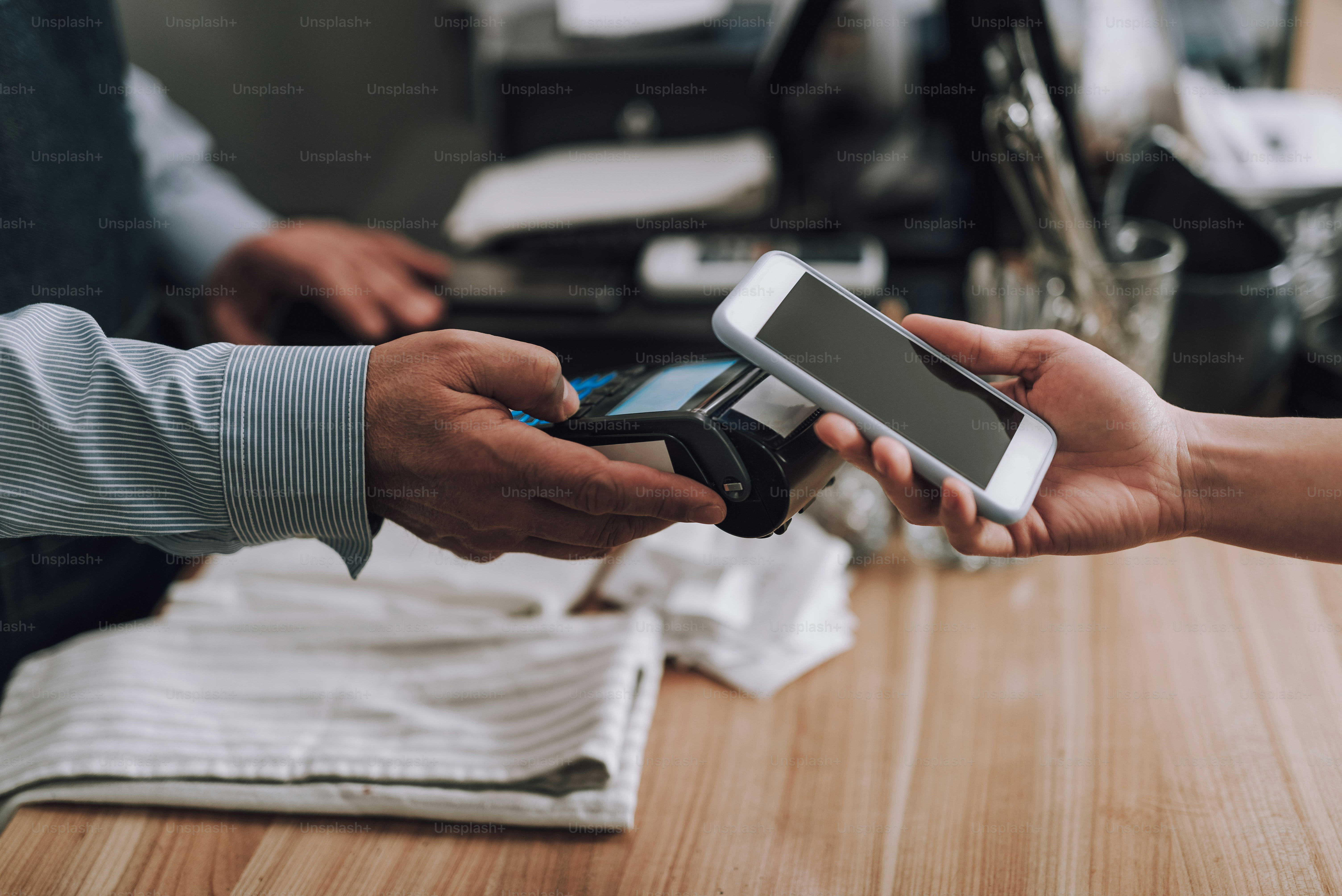 Primer plano de un trabajador masculino de la tienda que usa la terminal para el pago sin contacto mientras el cliente sostiene el teléfono inteligente