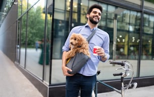 Handsome young man sitting on bike and holding coffee cup on street with dog