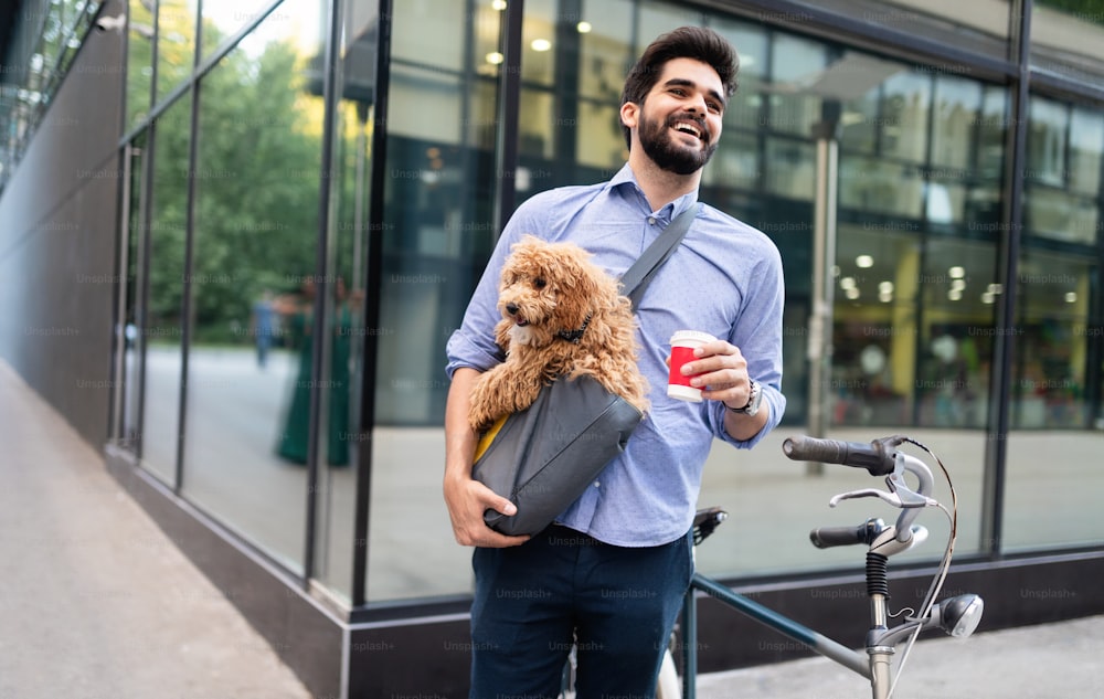 Handsome young man sitting on bike and holding coffee cup on street with dog